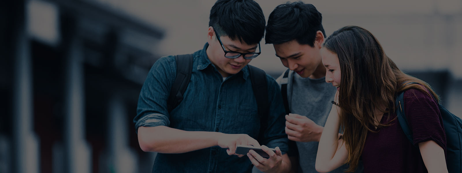 A male student showing two other students something on his mobile phone