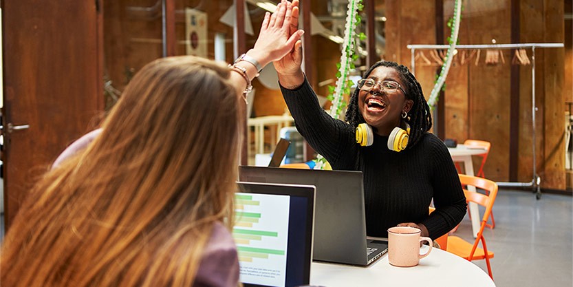 Professionals collaborate on laptops and share a celebratory high five