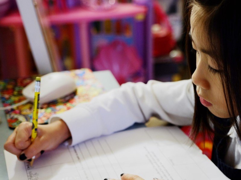 Focused girl doing homework at home and writing down in notebook